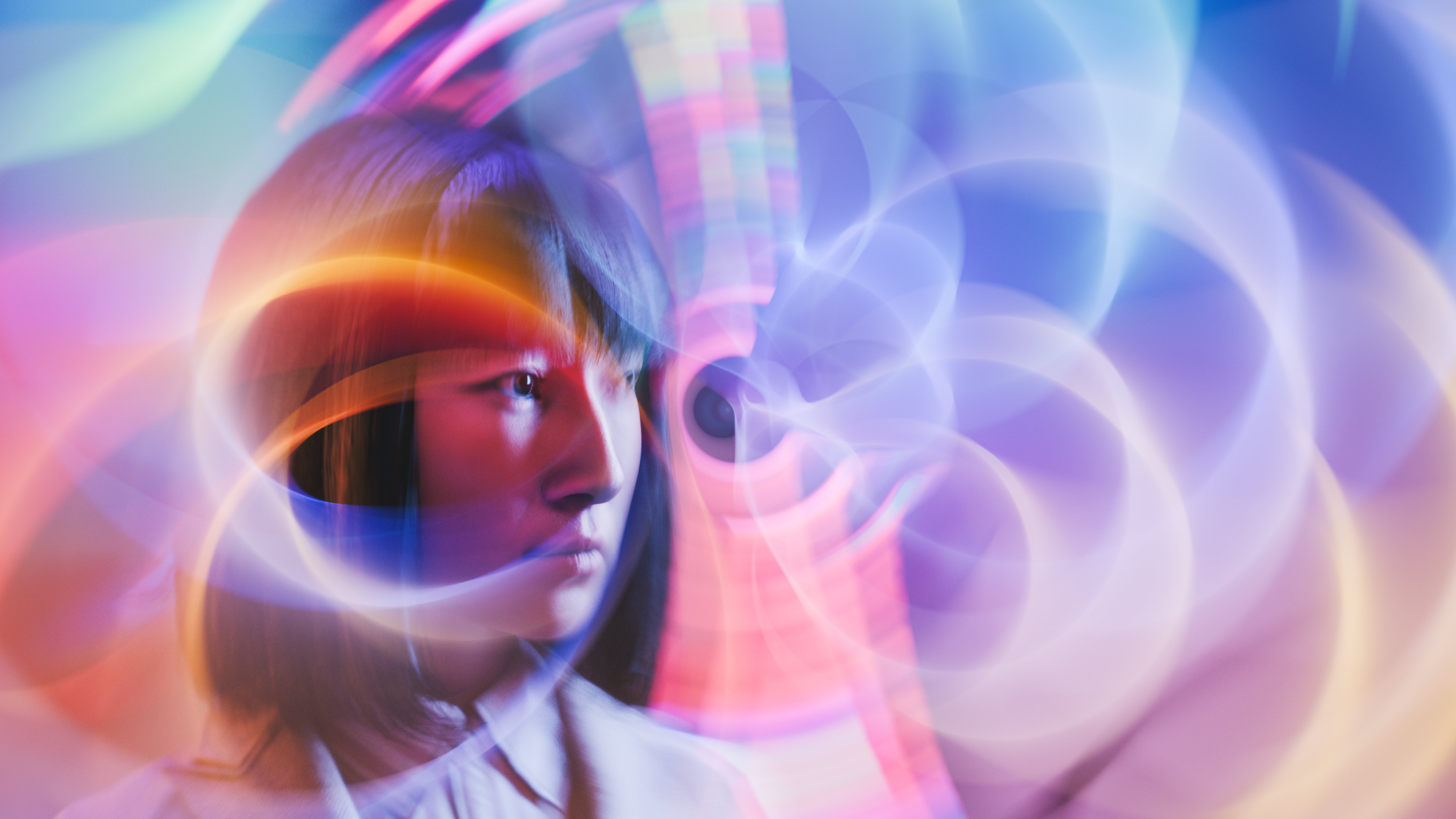 Abstract, digitally enhanced portrait of a person in profile,  overlaid with swirling, translucent light patterns in shades of blue, purple and white. The background is soft and blurred, with concentric, wave-like shapes suggesting motion or data flow. The overall composition combines human imagery with futuristic, technology-inspired visual elements.